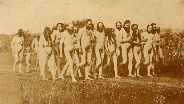 Eine Gruppe nackter Menschen geht auf einem Feldweg entlang.