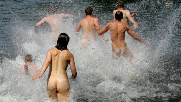 Mehrere nackte Personen rennen ins Wasser und erzeugen Spritzer.