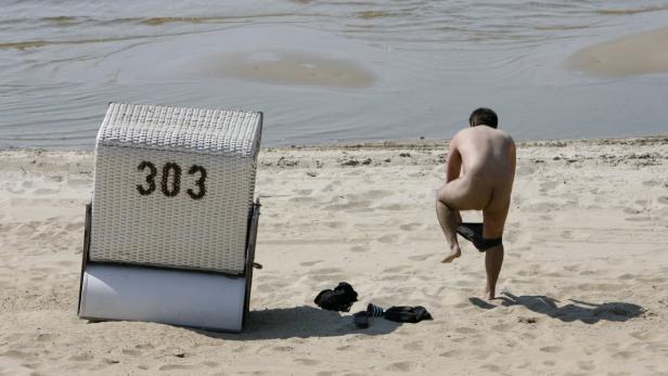 Ein Mann zieht sich am Strand neben einem Strandkorb mit der Nummer 303 um.