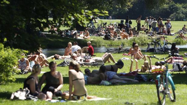 Viele Menschen entspannen sich an einem sonnigen Tag auf einer Wiese am Ufer eines Flusses.