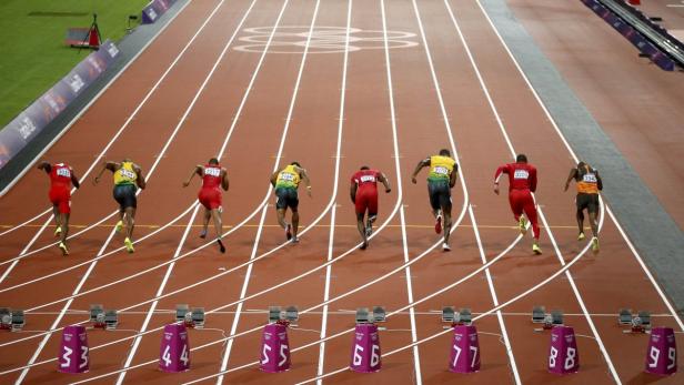 Leichtathleten starten bei einem Rennen auf einer roten Laufbahn.