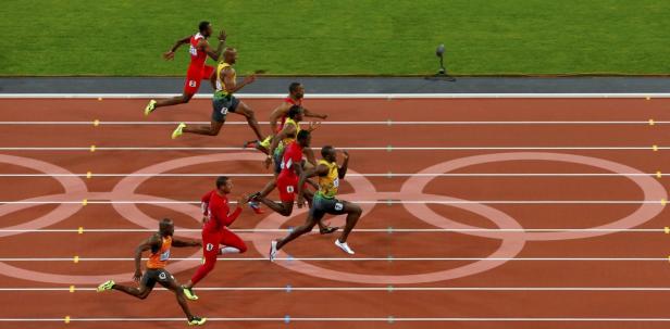 Mehrere Sprinter laufen auf einer roten Bahn mit den olympischen Ringen.