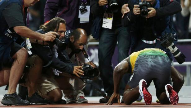 Usain Bolt kniet nach einem Rennen vor einer Gruppe von Fotografen.