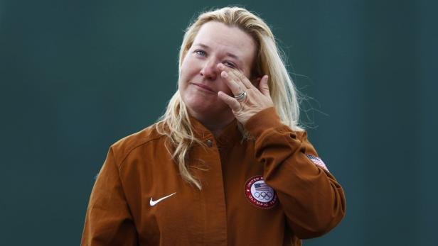 Eine Frau im braunen Olympiateam-Jacke wischt sich eine Träne aus dem Auge.