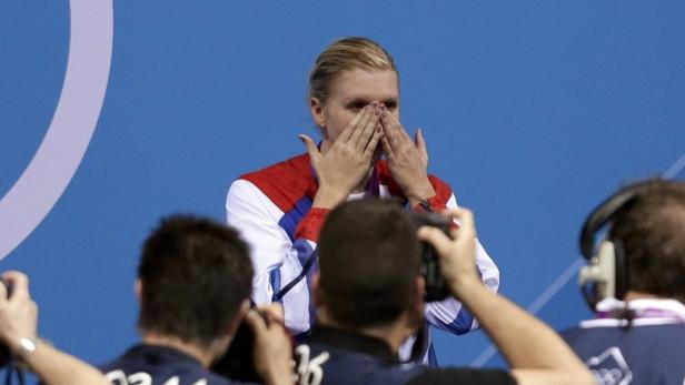Eine Sportlerin mit einer Medaille weint vor Freude, während sie von Fotografen umgeben ist.