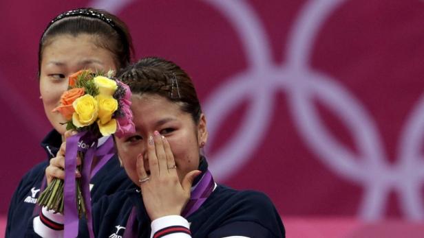 Eine Tischtennisspielerin weint gerührt mit einem Blumenstrauß vor dem Hintergrund der Olympischen Ringe.