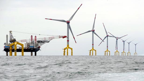 Eine Reihe von Windkraftanlagen auf See, mit einer Installationsplattform im Vordergrund.