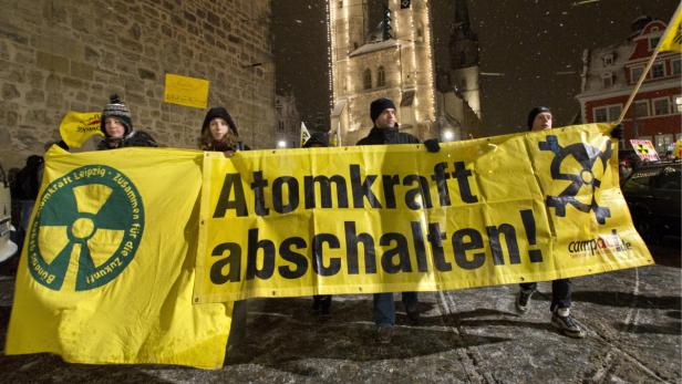 Menschen demonstrieren mit gelben Bannern gegen Atomkraft in einer Stadt bei Nacht.