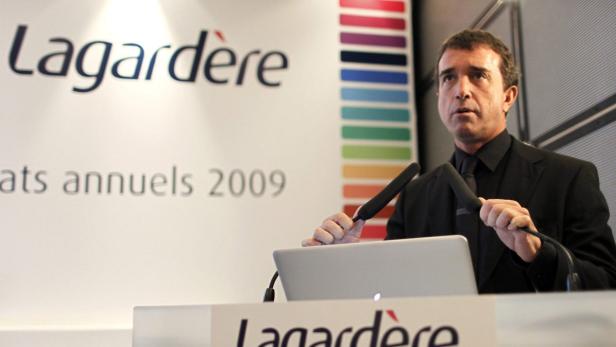 Ein Mann in einem schwarzen Anzug hält eine Rede vor einem Lagardère-Logo.