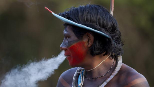 Ein indigener Mann mit Gesichtsbemalung raucht.
