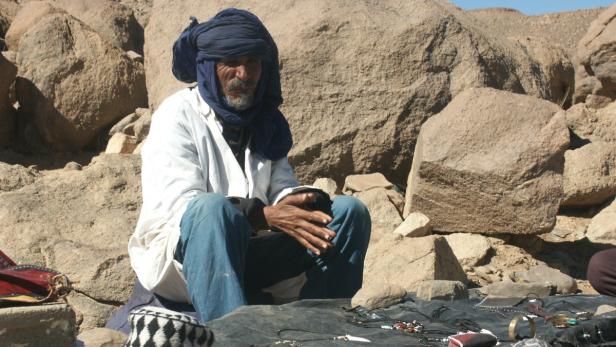 Ein Tuareg-Mann sitzt vor Felsen und verkauft Schmuck.