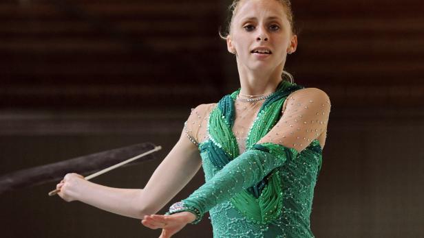 Eine rhythmische Sportgymnastin mit einem Band in einem grünen, glitzernden Anzug.