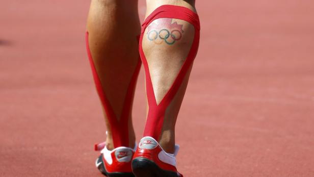 Die Beine eines Athleten mit rotem Tape und einem Tattoo der olympischen Ringe mit Ahornblatt.