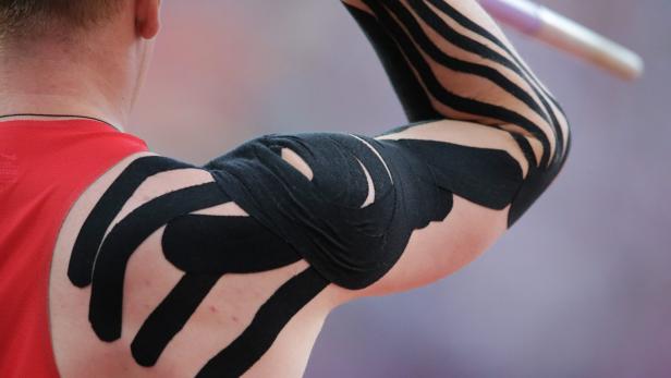 Der Arm eines Sportlers mit schwarzem, therapeutischem Tape beim Speerwerfen.