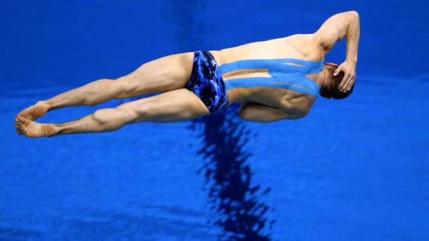 Ein männlicher Schwimmer mit blauem Tape taucht ins blaue Wasser.