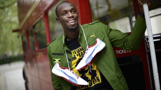 Usain Bolt posiert mit Spikes vor einem roten Doppeldeckerbus.