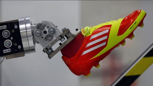 Ein rot-gelber Fußballschuh wird von einem Roboterarm gehalten.