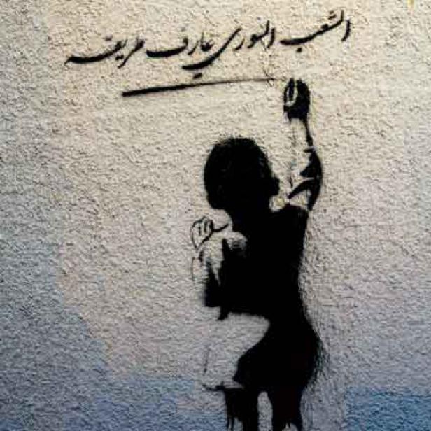 Ein Graffiti zeigt eine Person, die arabische Schriftzeichen an eine Wand malt.