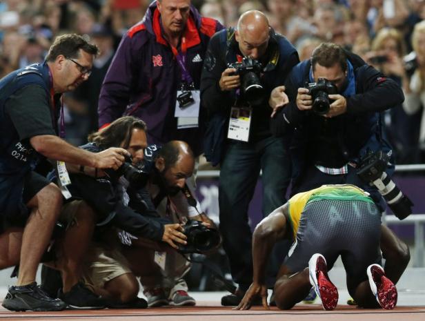Usain Bolt kniet nach einem Rennen umringt von Fotografen auf der Bahn.
