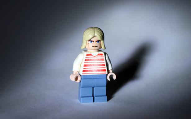 Eine Lego-Figur mit blonden Haaren, einem rot-weiß gestreiften Hemd und blauen Hosen steht im Licht.