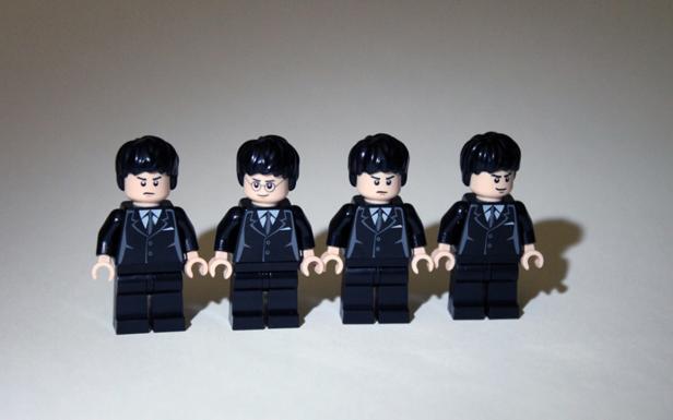 Vier LEGO-Figuren in schwarzen Anzügen stehen nebeneinander.