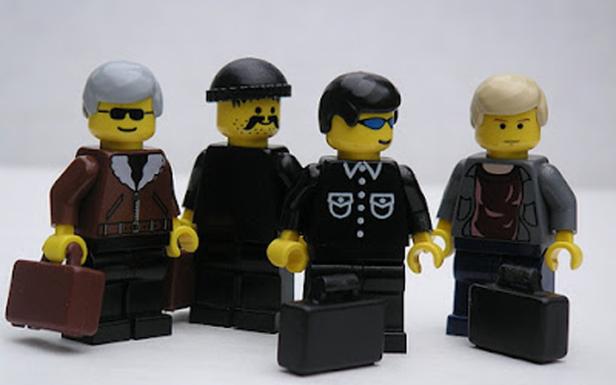 Vier Lego-Figuren in Anzügen halten Aktenkoffer.