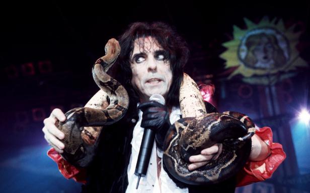 Alice Cooper hält eine Boa constrictor um seinen Hals und ein Mikrofon in der Hand.