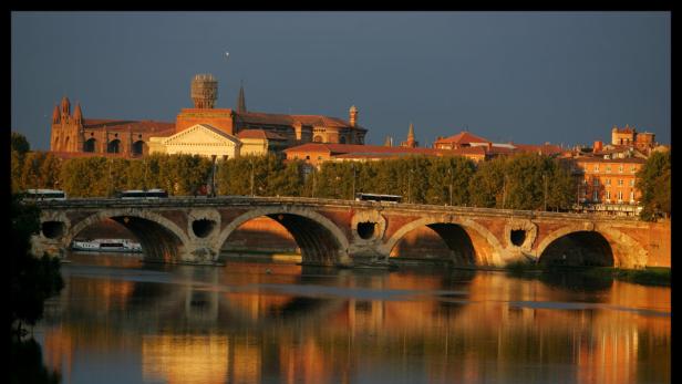 Die Pont Neuf Brücke in Toulouse spiegelt sich im Wasser der Garonne.