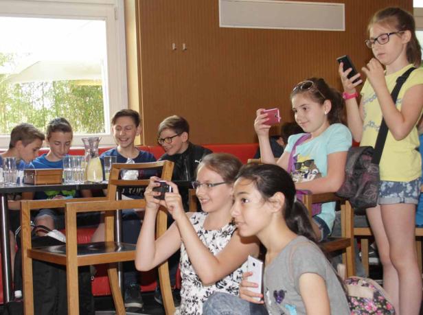 Eine Gruppe von Kindern sitzt und macht Fotos mit ihren Handys.