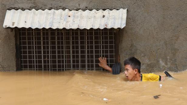 Ein junger Mann schwimmt durch das hochwasserartige Wasser vor einem vergitterten Fenster.