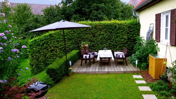 Ein gepflegter Garten mit Rasen, Blumen und einer Sitzecke mit Sonnenschirm.