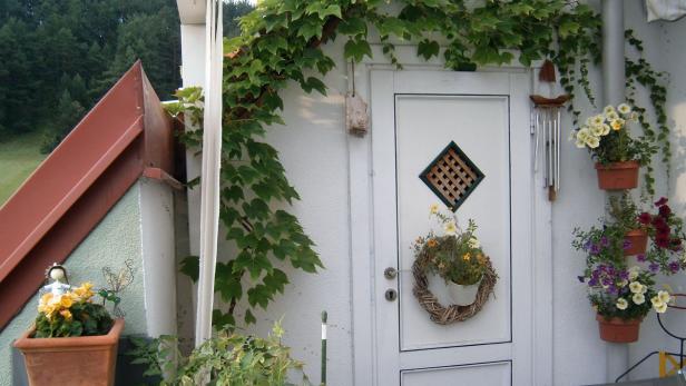 Eine Haustür ist mit einem Blumenkranz und hängenden Blumentöpfen geschmückt.