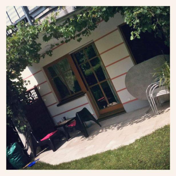 Eine Terrasse mit Tisch, Stühlen und einer Weinrebe, die überdacht ist.