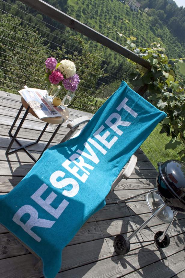 Ein Liegestuhl mit einem Handtuch mit der Aufschrift „Reserviert“ auf einer Holzterrasse.
