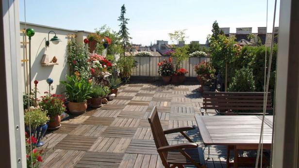 Ein begrünter Dachgarten mit Holzboden, Tisch und Bank lädt zum Verweilen ein.