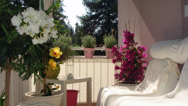 Ein sonniger Balkon mit blühenden Pflanzen und einem weißen Sofa.