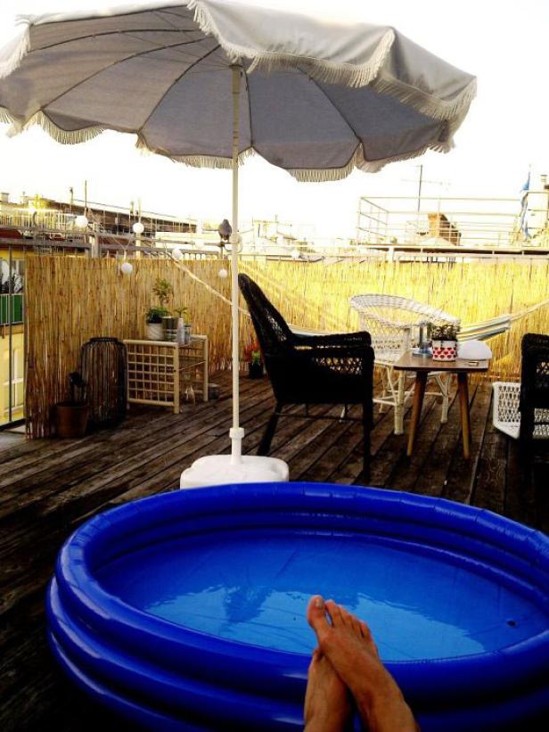 Ein blauer Pool steht auf einer Dachterrasse mit Sonnenschirm und Liegestuhl.