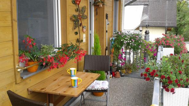 Ein Tisch mit zwei Tassen steht auf einem blumengeschmückten Balkon.