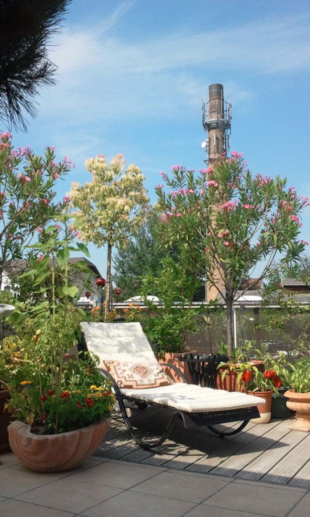 Ein Liegestuhl steht auf einer Dachterrasse, umgeben von Pflanzen und einem Schornstein im Hintergrund.