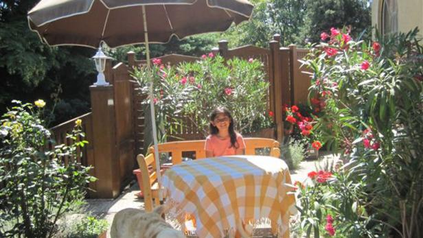 Ein junges Mädchen sitzt an einem Tisch mit karierter Decke in einem blühenden Garten.