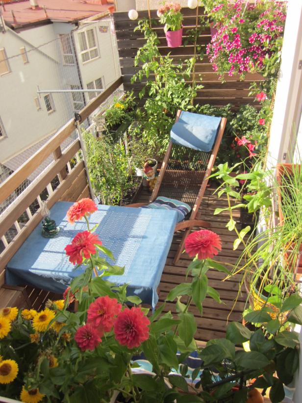 Ein blühender Stadtbalkon mit Tisch, Stuhl und vielen Pflanzen.