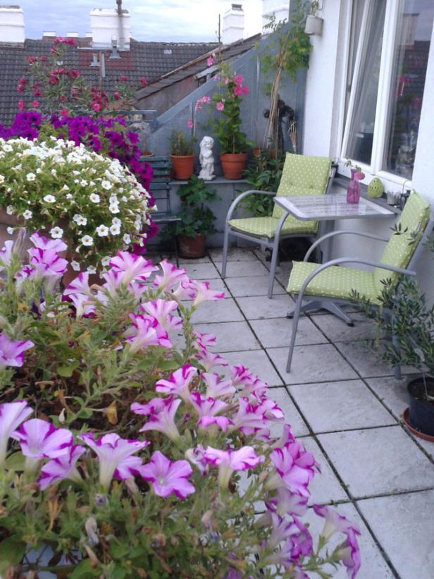 Ein blühender Balkon mit Blumen, Stühlen und einem kleinen Tisch.
