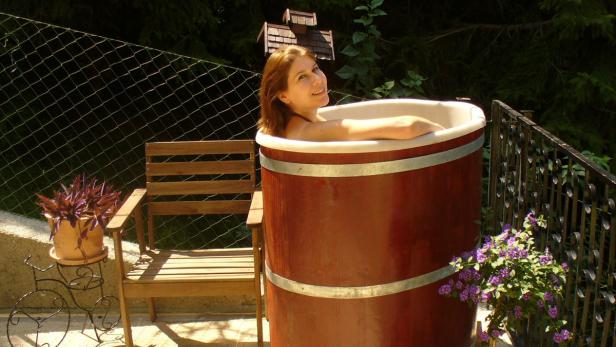 Eine Frau entspannt in einer hölzernen Badewanne im Freien.