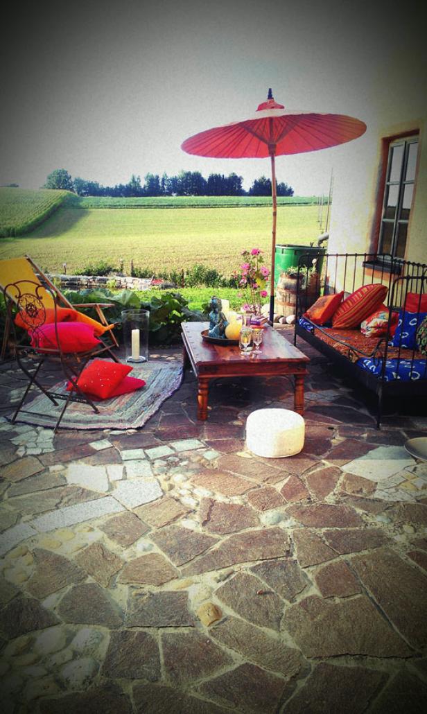 Einladende Terrasse mit rotem Sonnenschirm und Blick auf eine grüne Landschaft.