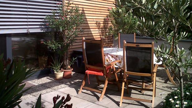 Ein Gartentisch mit Stühlen auf einer Terrasse mit Pflanzen und einem Holzzaun.