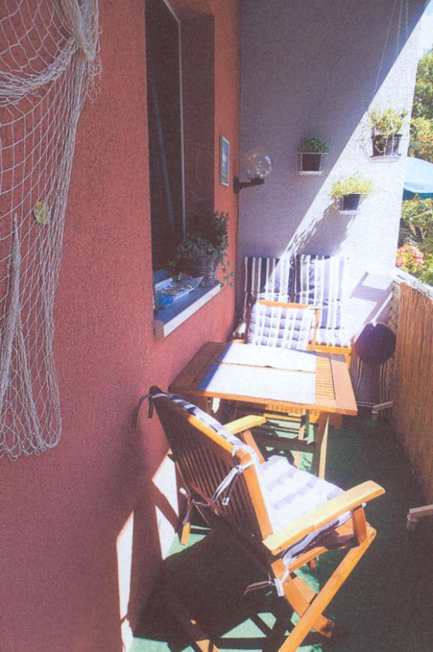 Einrichtung auf einem kleinen Balkon mit Tisch, Stühlen und maritimer Dekoration.