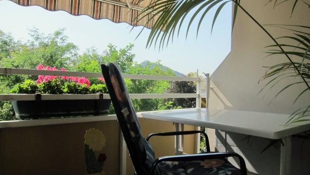 Ein Tisch und ein Stuhl stehen auf einem Balkon mit Blick auf grüne Bäume.