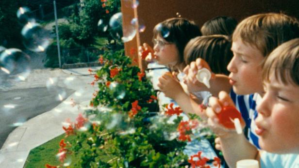 Eine Gruppe Kinder pustet Seifenblasen vor einem Blumenkasten.