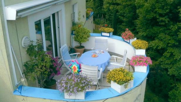 Ein blauer Tisch und Stühle stehen auf einem blumengeschmückten Balkon.