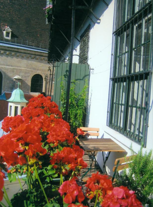 Ein Tisch und Stühle stehen auf einem Balkon mit roten Geranien.